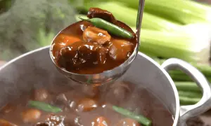 A ladle scoops tender, slow-cooked meat in rich gravy from a steaming pot. Perfect for learning jak dusić mięso.
