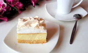 Pyszny sernik z bezą na białym talerzyku, obok filiżanka kawy i łyżeczka.
