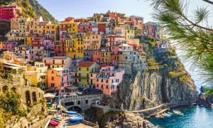 Färgstarka hus klättrar uppför klipporna vid havet i Italien. En vacker vy som ger fakta om Italien.