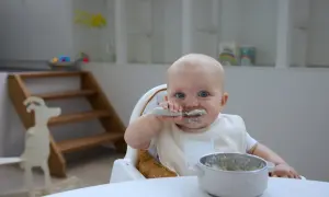 Ein süßer **Joghurt Baby** mit blauen Augen isst mit Löffel. Der Latz ist mit einer Ziege verziert.