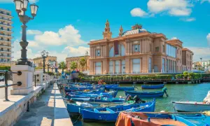 Barche blu ormeggiate nel porto, con il Teatro Margherita sullo sfondo. Un'immagine che cattura l'essenza di Bari e dintorni cosa vedere.