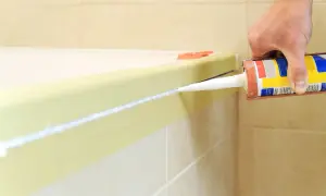 Dłoń trzymająca pistolet z silikonem, aplikująca biały uszczelniacz wzdłuż wanny. Poradnik jak usunąć silikon sanitarny.