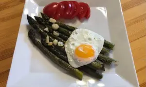 Szparagi z jajkiem sadzonym i pomidorem na białym talerzu.