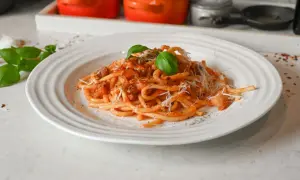 En tallrik med bucatini pasta i tomatsås, toppad med riven parmesan och färsk basilika. Ett perfekt bucatini pasta recept för en god middag.
