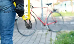 Osoba w dżinsach i czarnych rękawiczkach trzyma żółte nożyce do cięcia. W tle czerwony rower, który potrzebuje dobrego zabezpieczenia do roweru.