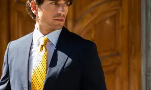Uomo elegante con giacca blu, camicia bianca e cravatta gialla con pois, annodata con un perfetto nodo Windsor.