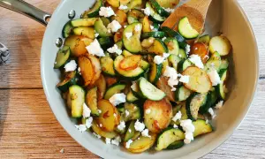Herzhafte zucchini pfanne mit goldbraunen Kartoffelscheiben und zerbröckeltem Feta, garniert mit frischen Kräutern.