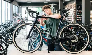Ein junger Mann prüft ein schwarzes Fahrrad in einem Geschäft, um zu entscheiden, welches Fahrrad zu ihm passt. Viele Fahrräder stehen im Hintergrund.
