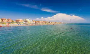 Słoneczny dzień nad morzem w Rzymie. Plaża pełna kolorowych leżaków i parasoli, ludzie kąpią się w krystalicznie czystej wodzie.