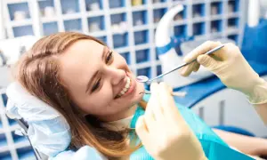 Uśmiechnięta kobieta u dentysty, badanie zębów lusterkiem i narzędziem.