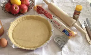 Préparation d'une tarte aux pommes simple : pâte sablée, pommes, citron, œuf, rouleau, emporte-pièces cœur et cannelle.