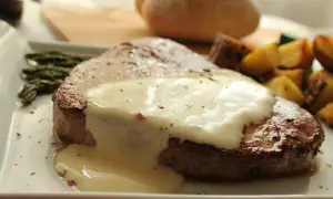 Filete redondo cubierto con una cremosa salsa blanca, acompañado de espárragos y patatas asadas.