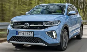 Niebieski VW T-Cross pędzi leśną drogą, odbijając drzewa w szybie.