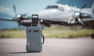 Szara walizka Peli Air na lotnisku, gotowa na lot czarterowy. Samolot w tle.