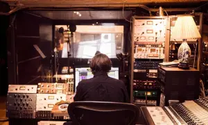 Producent muzyczny w studio, otoczony sprzętem, tworzy nową muzykę, być może z pomocą sztucznej inteligencji.