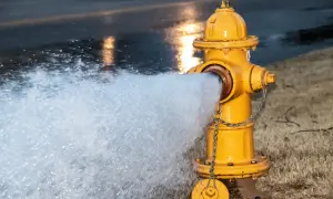 Żółty symbol hydrantu z łańcuchem, z którego tryska woda na mokrą ulicę.