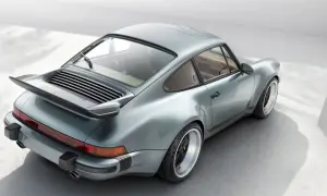 En ikonisk Porsche 80-tals coupé i ljusblått, med sin karaktäristiska bakvinge och breda fälgar.