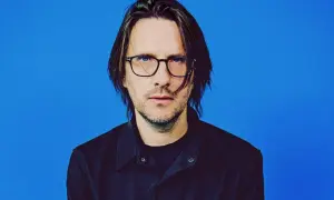 Steven Wilson, lider zespołu Porcupine Tree, w okularach i czarnej koszuli na niebieskim tle.