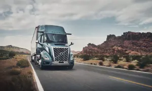 Un camion Volvo américain bleu foncé roule sur une route désertique sous un ciel nuageux.