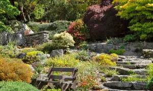 Ein terrassierter Garten am Hang mit Steinwegen und einer Holzbank. Bunte Blumen und Sträucher bedecken die Hänge.