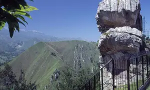 El idolo de peña tu, una roca con forma de perfil humano, vigila un paisaje montañoso verde y sereno bajo un cielo azul.
