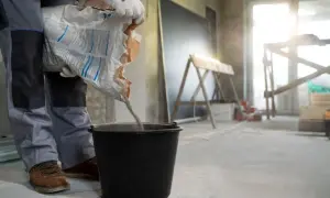 Budowlaniec wsypuje masę do wiadra, przygotowując wylewkę samopoziomującą. Minimalna grubość wylewki samopoziomującej jest kluczowa dla równej podłogi.