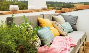 Sofá de palets con cojines coloridos y manta rosa, perfecto para una decoración chill out interiores. Velas aromáticas en la barandilla.