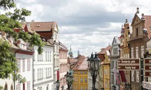 Ulica w Pradze z zabytkowymi kamienicami i latarniami. W oddali widać wieże, wskazujące na praga nietypowe atrakcje.