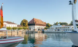 Boote am Bodensee, deutsche Flagge weht. Ein historisches Gebäude und ein Ausflugsschiff laden zu Konstanz Events ein.