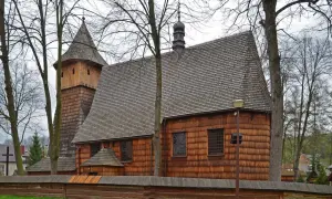 Drewniane kościoły południowej Małopolski: zabytkowa świątynia z wieżą i gontowym dachem, otoczona drzewami i drewnianym płotem.