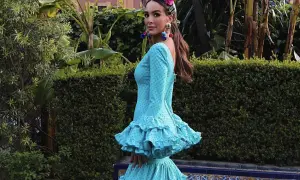 Una mujer luce un vestido de flamenca turquesa con lunares, adornado con volantes y una flor en la cabeza.