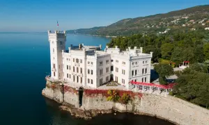 Vitt slott vid havet i Trieste, Italien, med en italiensk flagga på tornet.