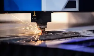 Precyzyjne cięcie aluminium przez laser, iskry rozbłyskują podczas pracy maszyny.