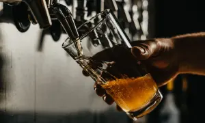Una mano tiene un bicchiere mentre la birra dorata viene spillata. La temperatura birra è perfetta per gustare questa bevanda rinfrescante.