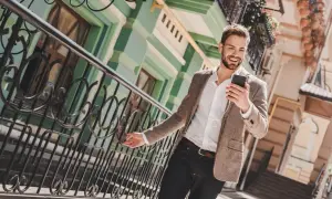 Ein Mann im casual chic Outfit mit Sakko und Jeans lächelt, während er auf sein Smartphone schaut.