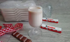 Pyszny likier z kinder czekoladek w kieliszku, obok batoniki i kawałek czekolady.