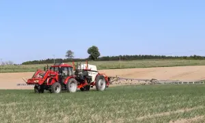 Czerwony traktor z opryskiwaczem polowym pracuje na polu. Tabela mieszania oprysków pomaga rolnikowi w precyzyjnym zabiegu.