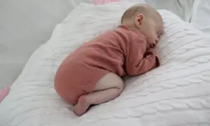 Sover sött på en vit stickad filt, en liten bebis i en rosa body. Hoppas bebisen inte hosta.