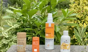 Quatre produits solaires, dont une crème solaire sans octocrylene, sont présentés sur un muret, entourés de verdure.