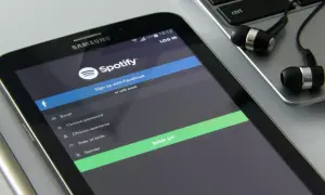 Ekran telefonu z aplikacją Spotify, formularzem rejestracji i słuchawkami na klawiaturze.