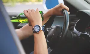 Ręce na kierownicy, jedna trzyma butelkę piwa. Kierowca w stanie nietrzeźwości kk.