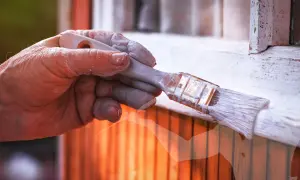 Main d'un peintre avec de la peinture blanche sur les doigts, tenant un pinceau. Astuces pour savoir comment enlever de la peinture sur les mains après le bricolage.
