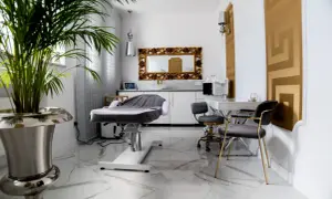 Nowoczesne gabinetowe wnętrze z fotelem do zabiegów wyszczuplających, lustrem w złotej ramie i eleganckimi krzesłami.