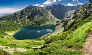 Bergsee in Polen, umgeben von grünen Hängen und schroffen Gipfeln. Die beste Reisezeit für solche Ausblicke ist der Sommer.