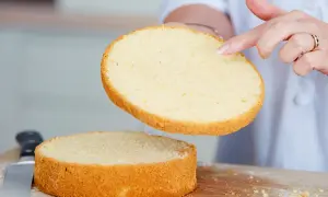 Perfekter tortenboden rezept: Eine Hand hebt eine goldbraune Kuchenschicht über eine zweite, die auf einem Holzbrett liegt.