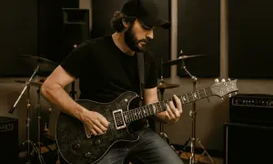 Mężczyzna w czapce z daszkiem gra na gitarze elektrycznej w studiu. Idealny obraz, by dowiedzieć się, jak zacząć grać na gitarze elektrycznej.