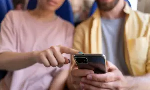 Pareja joven en un avión, compartiendo un teléfono. Quizás discutiendo sobre sus **relaciones parasociales** con influencers o celebridades.