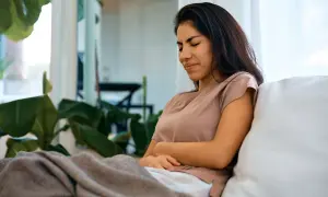 Frau mit Bauchschmerzen, vielleicht wegen Kreatin-Nachteile. Sie sitzt auf einem Sofa, zugedeckt mit einer Decke.