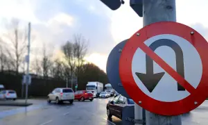 Znak drogowy zakaz zawracania na tle mokrej drogi i samochodów.