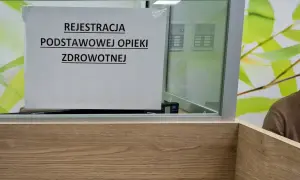 Tabliczka "Rejestracja podstawowej opieki zdrowotnej" w poczekalni. W tle widać fragment mężczyzny i zielone liście.